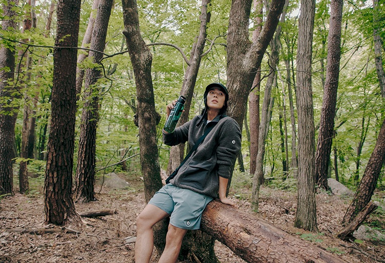 우거진 숲 속에서 나무에 걸터앉아 텀블러를 손에 쥔 남자모델